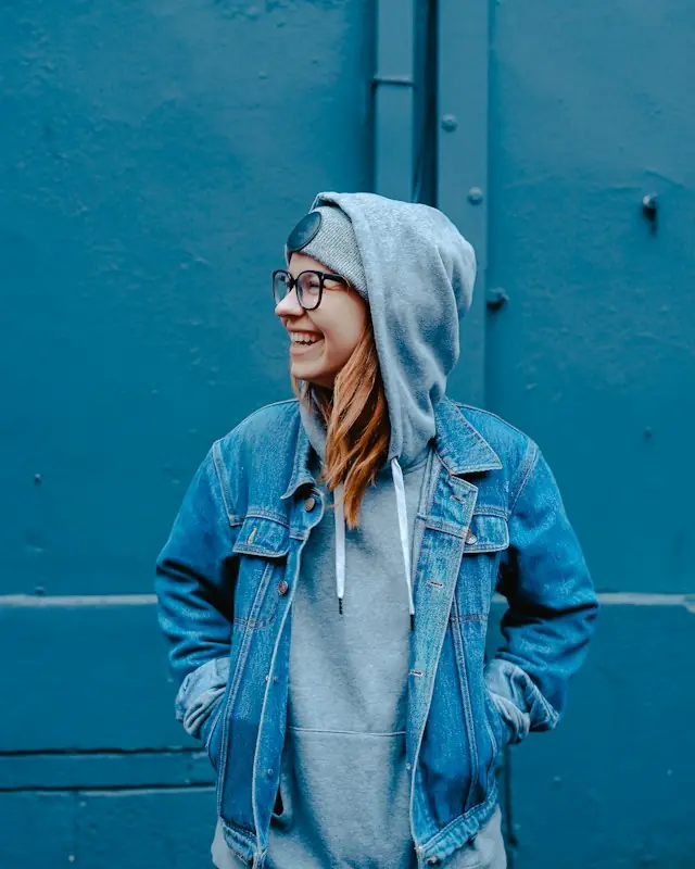 Student in a denim jacket and hoodie smiling on campus